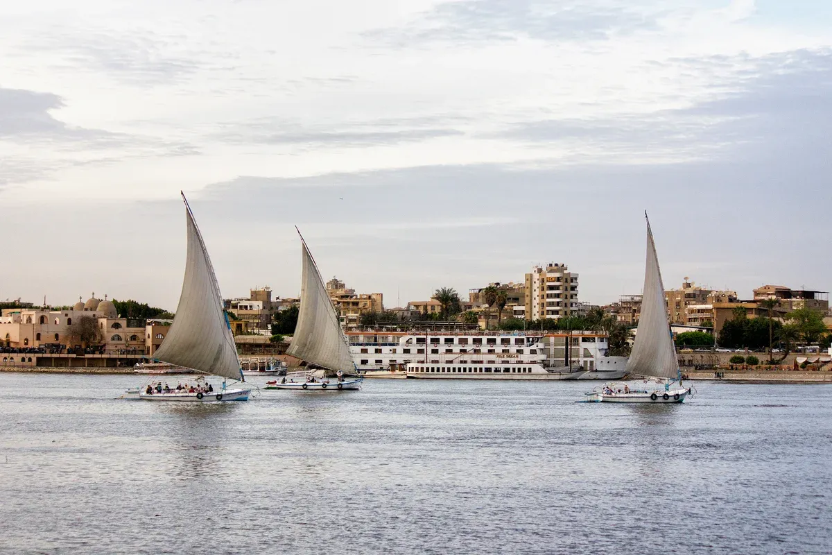 Three feluccas sailing on the Nile in front of a cruise ship on a Nile cruise day